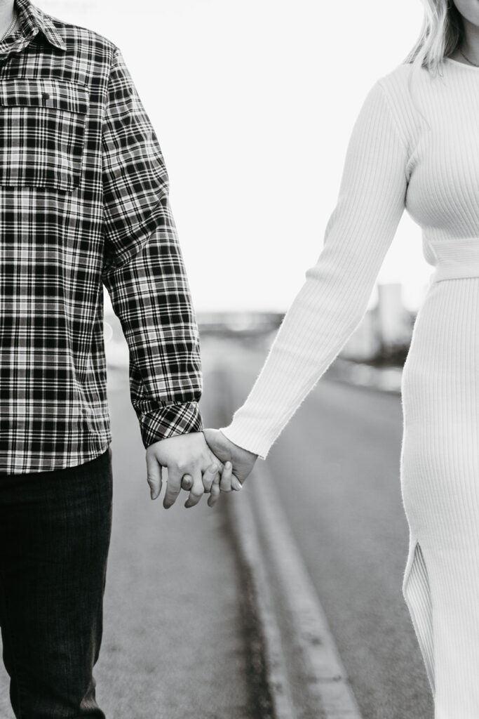 Black and white engagement photo of couple holding hands in the street
